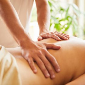 Closeup of a male massage therapist's hands working on the back of a woman on a table in his clinic